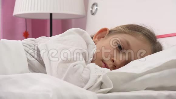 睡在床上的悲伤体贴的孩子不睡觉睡在卧室里醒来的女孩的脸视频的预览图