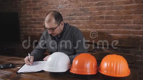 男领班坐在工地办公室的办公桌后面重新计算头盔视频的预览图