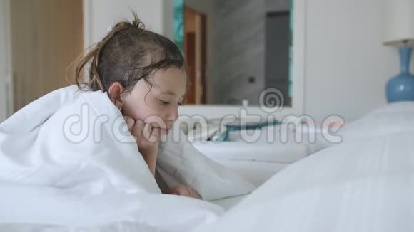 小女孩躺在毯子下在平板电脑上看动画片视频的预览图