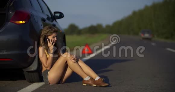 一个年轻女子打电话一辆坏车在路上紧急情况下停在车架上视频的预览图