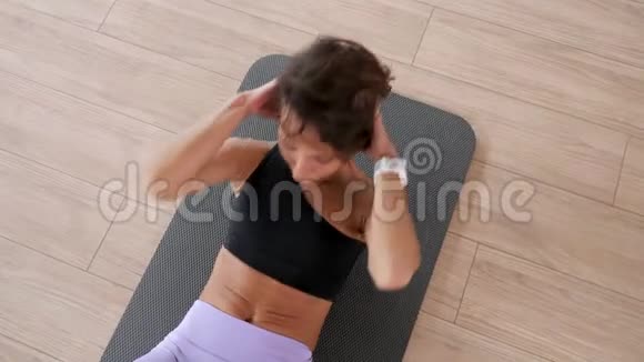 成熟的女人在健身房的垫子上慢慢地做腹肌紧缩运动视频的预览图