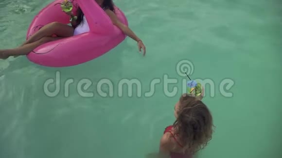 两个穿着泳衣的漂亮女朋友在游泳池里玩得很开心喝着鸡尾酒一个黑发女孩坐在视频的预览图