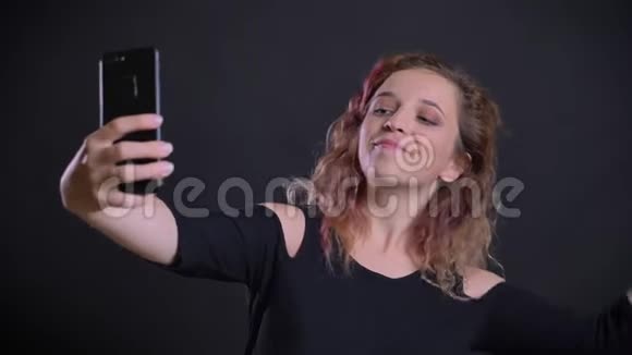 年轻的白种人女孩的肖像粉红色的头发愉快地在视频聊天使用智能手机在黑色背景视频的预览图