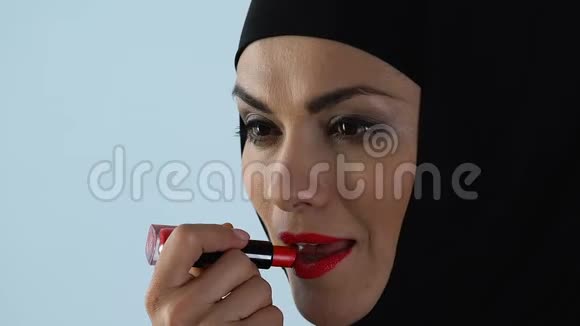 戴头巾的自信女人在镜子前涂红唇膏化妆视频的预览图