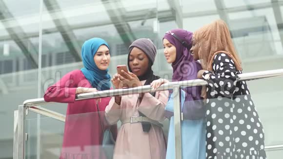 穆斯林多民族女孩看着非洲女人手中的智能手机视频的预览图