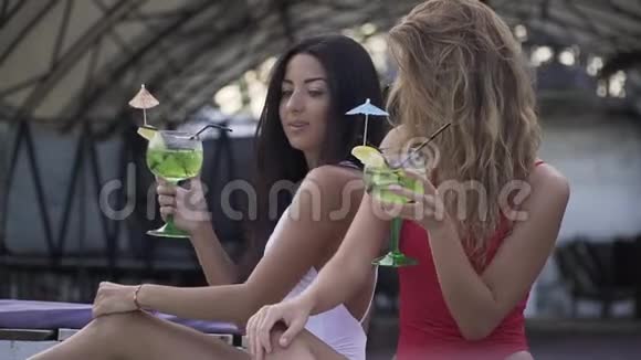 两个苗条漂亮的女孩点击眼镜喝鸡尾酒并在休息室玩得很开心两个女朋友视频的预览图