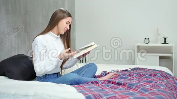 美丽的欧洲年轻女子坐在床上拿着有趣的书看书视频的预览图