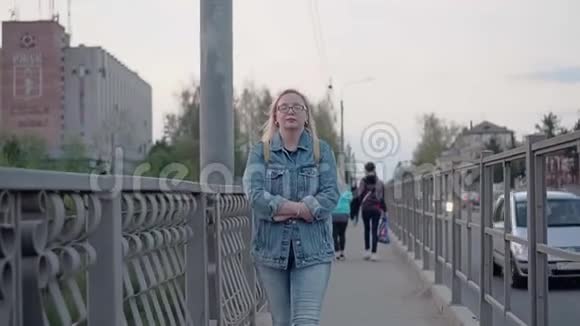 女孩走在傍晚的城市在桥上她把胳膊裹在袖子里试图保暖美丽的计划正在进行中视频的预览图