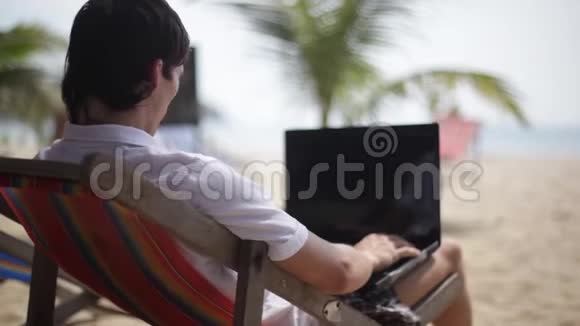 一个年轻的自由职业者在海滩上用笔记本电脑工作1920x1080个视频的预览图
