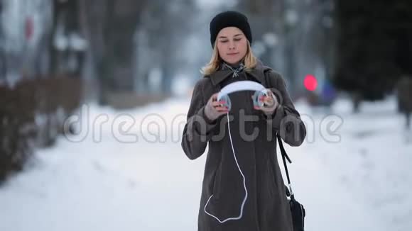 戴着耳机听音乐的女人走在冬天的城市小巷里视频的预览图