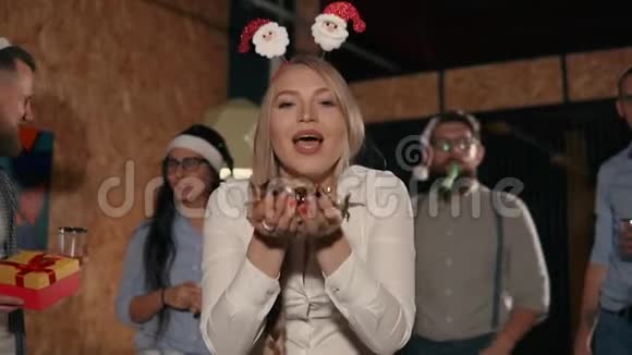 办公室圣诞派对上微笑的女孩吹着闪亮的五彩纸屑视频的预览图