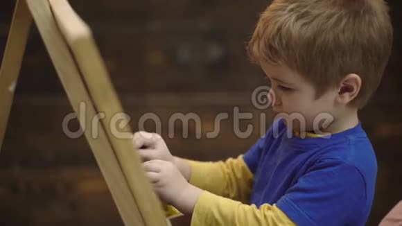 用粉笔在黑板上书写的男孩的特写可爱的幼儿男孩在木制背景上画黑板视频的预览图