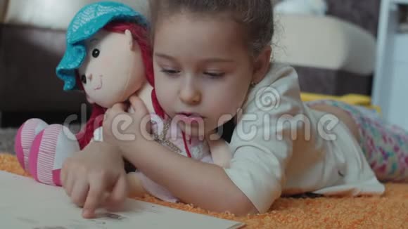 可爱的留着卷发的小女孩穿着孩子们睡衣躺在地板上的针织地毯上她自己在读一本视频的预览图