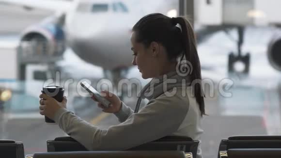 手里拿着外卖咖啡的女孩在机场用电话记录语音留言视频的预览图