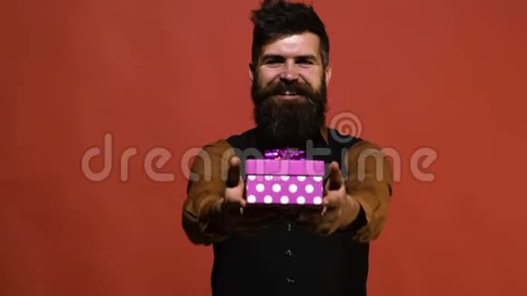 胡子男手里拿着新年礼物红色背景庆祝新年的概念男人送礼物视频的预览图
