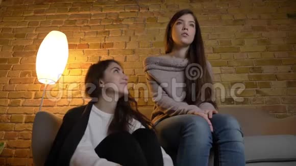 年轻白种人女孩坐在一起看电影的肖像在舒适的家庭氛围中积极娱乐视频的预览图
