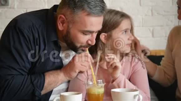 青春期的小女孩和她爸爸在咖啡馆里玩得很开心他们用冰块喝深红色果汁视频的预览图
