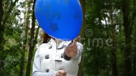 快活的女人站着在松松木里飘着一个蓝色的气球视频的预览图