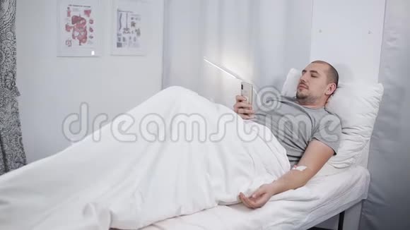 一个病人躺在医院病房的床上看着电话视频的预览图