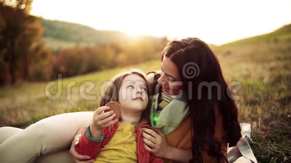 一位年轻的母亲带着一个小女儿在秋天的大自然中日落吃饼干视频的预览图