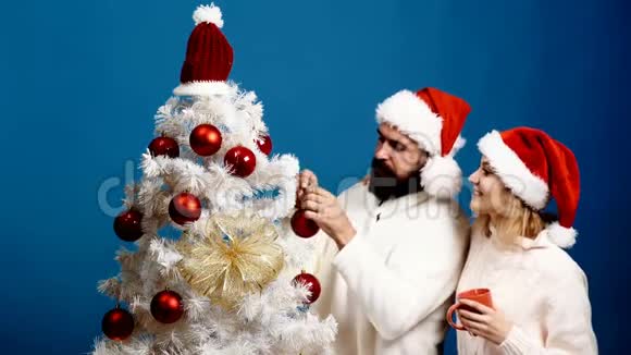 一对夫妇花时间装饰圣诞树戴着红帽子的大胡子男人和女孩圣诞节装饰视频的预览图