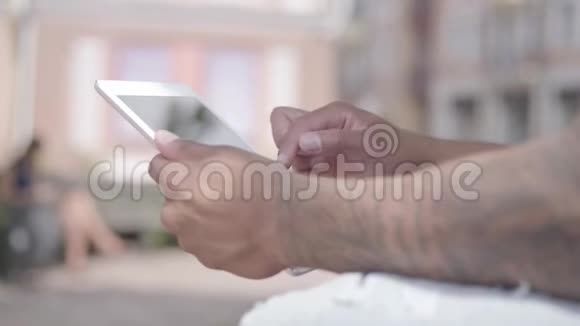 未被认出的中东男子在平板电脑上打字坐在街上的长凳上他把时间花在户外视频的预览图