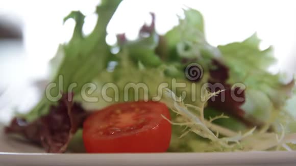 在一个盘子上倒入一杯橄榄油上面有绿色的生菜和西红柿视频的预览图