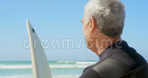 活跃的高加索人站在海滩上冲浪板的侧面景色视频的预览图
