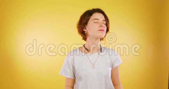 可爱的女孩在无线耳机里听音乐在黄色的背景下跳舞和微笑技术音乐视频的预览图