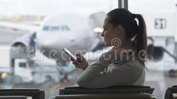 机场候机室内使用智能手机的年轻美女侧视窗外的飞机背景视频的预览图