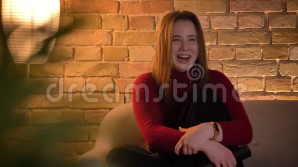 年轻活泼的白种人女性在电视上看喜剧的特写镜头坐在沙发上笑着笑视频的预览图