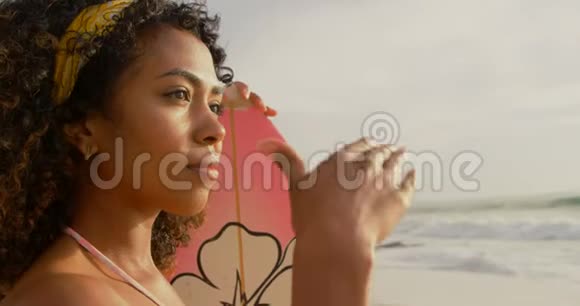 非洲裔美国女性冲浪者站在海滩上冲浪板的侧面景色视频的预览图