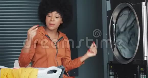 年轻快乐的非裔美国女人卷发滑稽地在自助式公共洗衣店跳舞视频的预览图