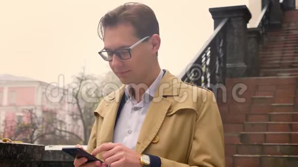 一幅美丽的白种人的特写肖像他在手机上浏览站在公园户外视频的预览图