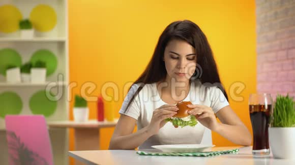 漂亮的女士咬着陈腐的汉堡喝苏打水不开心的顾客食堂视频的预览图
