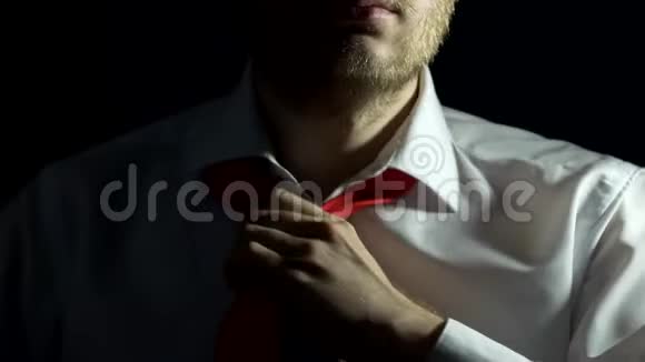一个留着胡须穿着白色衬衫的男人正在系领带并在他的衬衫上扣上纽扣特写黑色背景视频的预览图