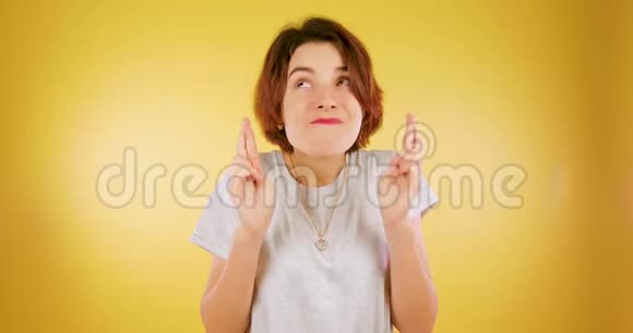 一个十几岁的女孩交叉手指在黄色的背景下等待了很多布鲁内特女孩等待结果视频的预览图