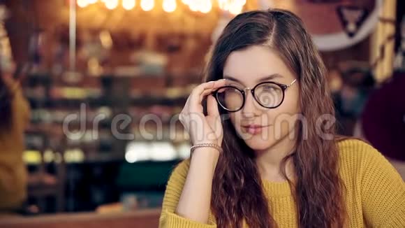 一个漂亮女孩在一家带眼镜的舒适咖啡店的肖像视频的预览图