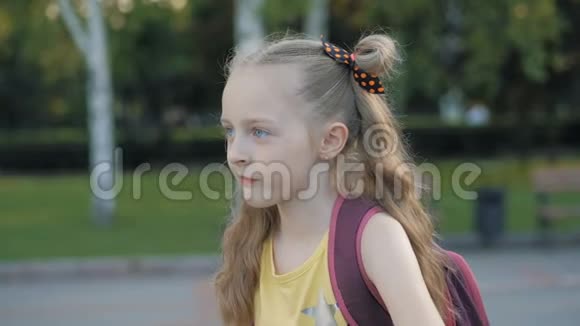 年轻的金发女孩背着背包在公园前面视频的预览图