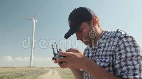 一个人在风力涡轮机的背景下控制着一个无人驾驶飞机对地形进行检查的概念视频的预览图
