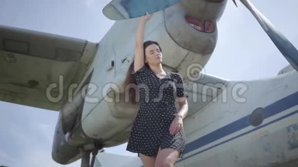 快乐的年轻黑发女孩穿着黑色的裙子看着摆在白色飞机前面的相机触摸着视频的预览图
