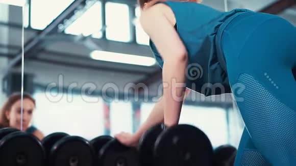 后景年轻的健身女孩在一面巨大的镜子前用哑铃做运动视频的预览图