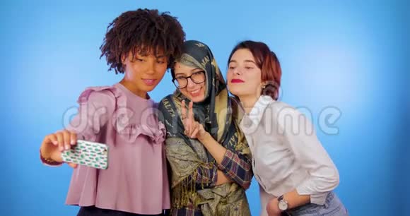 非洲欧洲和穆斯林妇女自拍摆出孤立的蓝色背景国际可爱科技视频的预览图