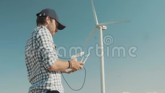 一个人在风力涡轮机的背景下控制着一个无人驾驶飞机对地形进行检查的概念视频的预览图