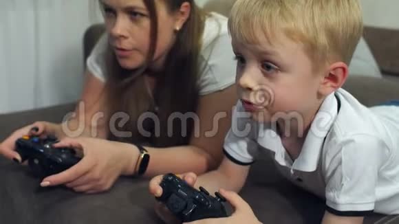 母亲和儿子玩电脑游戏玩操纵杆躺在沙发上视频的预览图