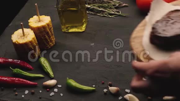 年轻女子将肉排放在餐桌上的特写视频配上西红柿玉米大蒜迷迭香视频的预览图