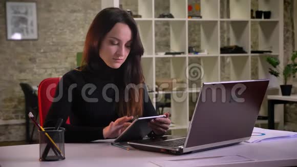 有魅力的年轻黑发女商人在办公室里专心工作与平板电脑的肖像视频的预览图