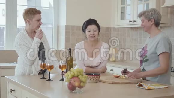 成熟的女人在家里聊天站在厨房中间的现代餐桌旁一位女士在切苹果视频的预览图