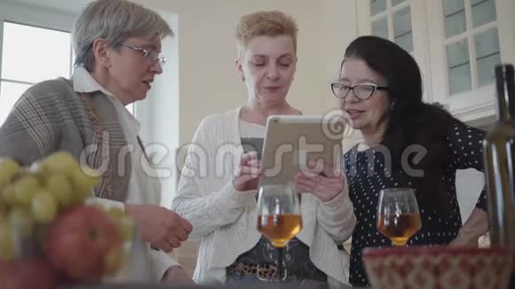 三个成熟的女朋友在平板电脑上观看有趣的东西的肖像并正在积极讨论成人视频的预览图