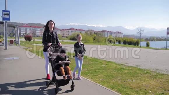 妈妈带着婴儿车和两个孩子在街上散步视频的预览图